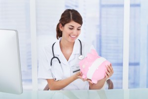 Young female doctor looking at piggybank with bandage in clinic